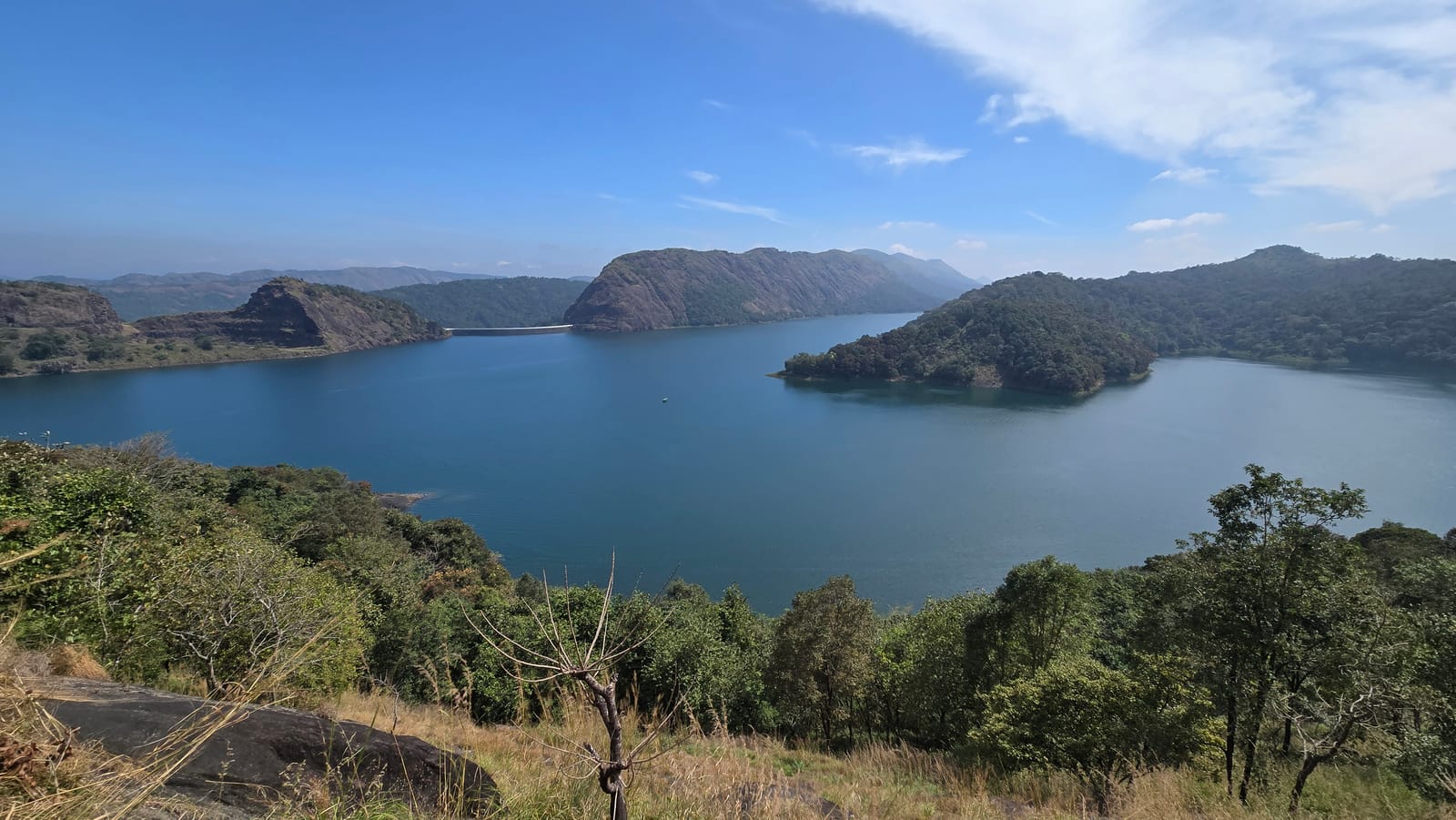 A wide blue reservoir among forested hills under a clear sky, with a dam wall in the distance